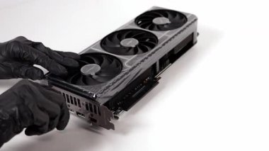 Siyah eldiven giyen bir kişi, ASUS GeForce RTX grafik kartından beyaz bir yüzey üzerinde üç pervaneli soğutma sistemi içeren koruyucu filmi dikkatlice çıkarır.