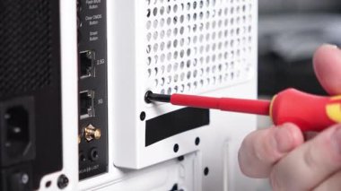 Birisi tornavida kullanarak beyaz bir bilgisayar kutusuna vida takıyor. Görüntü arka paneli ethernet, ses portları ve havalandırma delikleriyle gösteriyor.