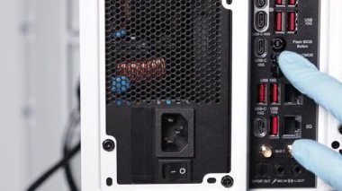 Modern bir masaüstü anakartının arka IO panelindeki Clear CMOS ve Flash BIOS düğmelerini gösteren mavi eldivenli bir kişi.