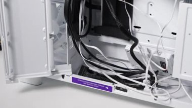 Sistem montajı sırasında görünür SSD parantezi, güç kabloları, veri bağlayıcıları ve etiketleri olan organize kablo yönetimini gösteren beyaz bir PC dosyasının içi