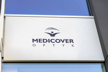 Poznan, Polonya - 15 Mart 2025: modern beyaz paneldeki sağlık örtüsü logosu üzerinde soyut göz sembolü ve mavi gökyüzü yansıması gözlükçü kliniğinin dış duvarında gündüz gözüyle görülebiliyor.