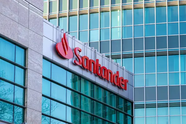 Poznan, Polonya - 15 Mart 2025: Santander Bankası logosu şehrin finans bölgesindeki modern cam ofis cephesinde, mavi renkli camlarda ağaçların ve gökdelenlerin yansımaları var.