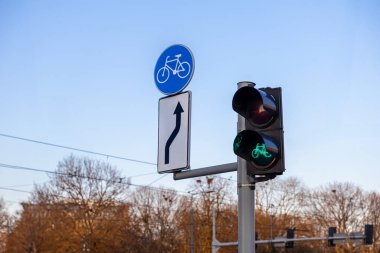 Açık bir günde arka planda ağaçlar ve elektrik hatları olan cadde kavşağında yeşil ışık ve bisiklet yolu işareti olan bisiklet trafiği.