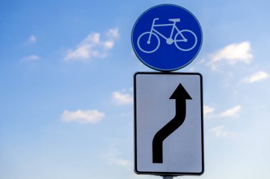 Bisiklet yolu trafik işareti ve eğri yön oku mavi gökyüzünün altında güneşli bir günde dağılmış bulutlarla bisiklet sürücüleri için yol altyapısı sembolü
