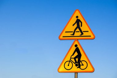 Sarı uyarı yol işaretleri ile yaya geçidi ve üçgen panellerde bisiklet sembolü açık mavi gökyüzüne karşı kentsel taşımacılık alanında açık mavi