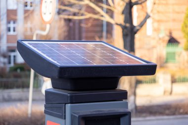 Modern Avrupa şehrinde güneşli bir günde arka planda bulanık hız limiti işareti ve konut mimarisi olan akıllı parkmetrenin üstündeki güneş panelini kapat