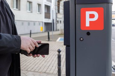 Şehir caddesinde güneş enerjisiyle çalışan parkmetrenin önünde cüzdan tutan adam, şehir bölgesinde nakit ödemeye hazırlanıyor, el ve makine yakın çekim görüntüsü