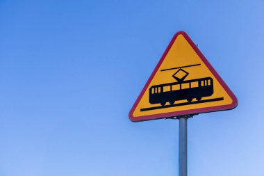 Tramvay yoluna yaklaşan yol işareti açık mavi gökyüzüne karşı kırmızı kenarlı parlak sarı bir üçgen üzerinde kentsel ulaşım alanında.