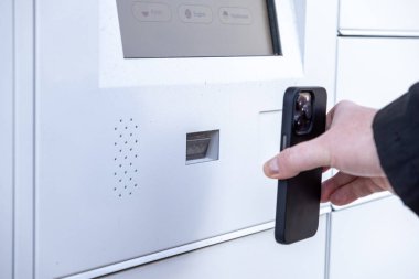 Modern iletişim süreci sırasında QR kodu ya da uygulama kullanarak paketi almak için akıllı telefonu beyaz parsel dolap ekranında tarayan adam