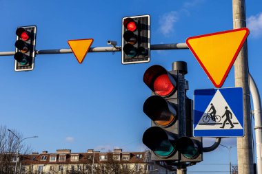 Şehir caddesinde mavi gökyüzü arka planı ve yaya geçidi sembolü olan trafik ışıkları ve yol işaretleri.
