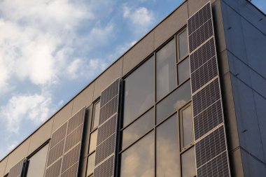 Dikey güneş panelleri ve yumuşak akşam gökyüzünü yansıtan büyük cam pencereli modern bina cephesi