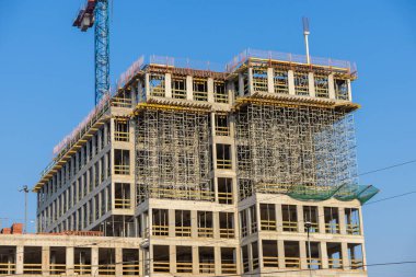 Şehir geliştirme projesinde güneşli bir günde mavi gökyüzüne karşı inşaat halindeki modern beton ofis binası.