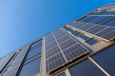 Açık mavi gökyüzü altında yenilenebilir enerji ve sürdürülebilirlik cephesinde kurulu güneş panelleri olan modern bina düşük açılı çevre dostu mimari