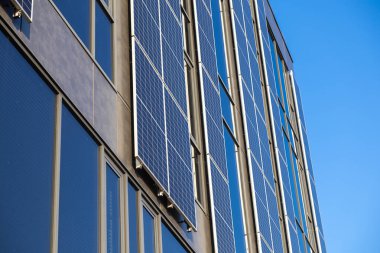 Güneş panelleri, açık mavi gökyüzünü, yenilenebilir enerjiyi ve sürdürülebilir kentsel mimari arka planı yansıtan yüksek modern binaya kurulmuştur.