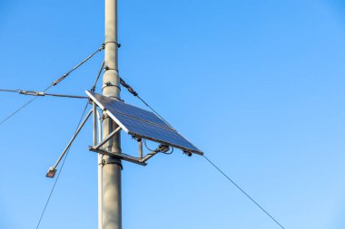 Metal sokak kutbuna bağlı modern güneş paneli açık mavi gökyüzüne karşı elektrik kabloları, akıllı şehir altyapısı için sürdürülebilir enerji çözeltisi