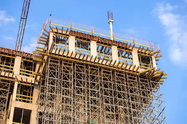 Güneşli bir günde parlak mavi gökyüzüne karşı çelik iskelesi ve beton iskelesi olan yüksek binalar inşa ediliyor.
