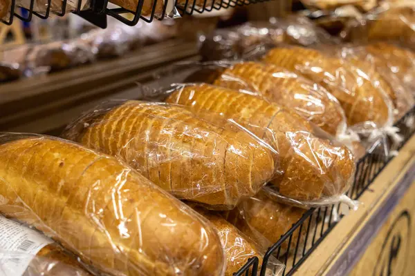 Pastanenin rafında şeffaf ambalajda taze fırınlanmış beyaz ekmek somunları. Sıcak ışıklandırma ve yakın çekimde altın kabuklar.