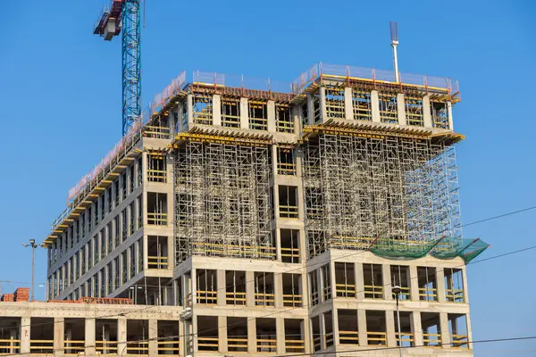 Şehir geliştirme projesinde güneşli bir günde mavi gökyüzüne karşı inşaat halindeki modern beton ofis binası.