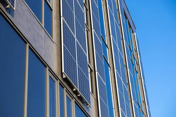 Güneş panelleri, açık mavi gökyüzünü, yenilenebilir enerjiyi ve sürdürülebilir kentsel mimari arka planı yansıtan yüksek modern binaya kurulmuştur.