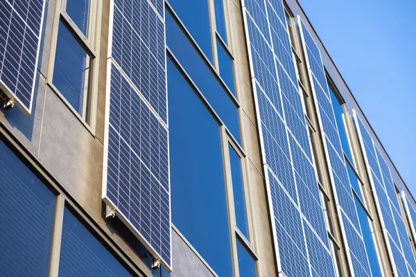 Güneşli bir günde yenilenebilir enerji üreten modern ofis binasındaki güneş panellerinin dikey görüntüsü mavi gökyüzü ve kentsel mimaride cam yansımaları