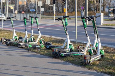 Poznan, Polonya - 22 Mart 2025: Paylaşılan Lime elektrikli scooter 'lar bisiklet yolunun yakınındaki yol kenarındaki çimlere ve güneşli bir günde şehrin kavşağına park edilmiş, çevre dostu kentsel hareketliliği temsil ediyor