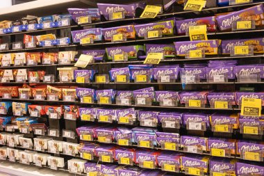 Poznan, Polonya - 22 Mart 2025: Polonya perakende satış mağazası şeker reyonundaki fiyat etiketleri ve tanıtım etiketleriyle süpermarket raflarında düzenlenmiş renkli ambalajlı Milka çikolataları