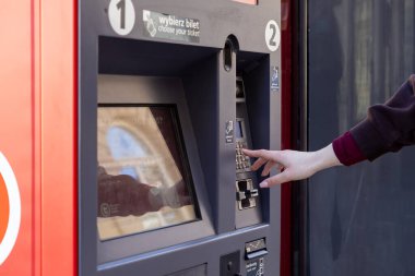 Varşova, Polonya - 3 Nisan 2025: Varşova, Polonya 'da toplu taşıma bilet otomatı ile etkileşime geçen bir kadın. Terminalde dokunmatik ekran, tuş takımı ve kart ödeme seçenekleri yer alıyor.