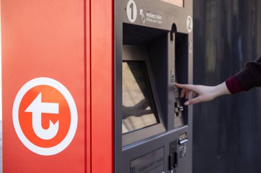 Varşova, Polonya - 3 Nisan 2025: Kırmızı bir toplu taşıma otomatı kullanan bir kadının yakın çekimi. Makinenin dokunmatik ekran ve kart ödeme sistemi var.