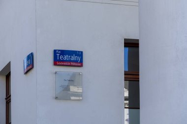 Varşova, Polonya - Nisan 03, 2025: Plac Teatralny tabelası ile sokak manzarası beyaz bir duvara asılmış, yanında tarihi bir plaket, bir pencere ve yumuşak gün ışığında büyük bir sütun.