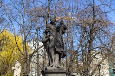 Varşova, Polonya - 3 Nisan 2025: Heykel taşıyan kadın heykelinin klasik taş heykeli, açık bahar gökyüzünün altında çıplak ağaçlarla çevrili bir şehir parkında bir heykel üzerinde duruyor.