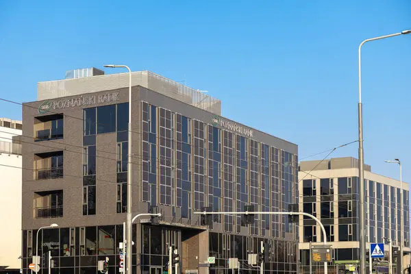 Poznan, Polonya - 22 Mart 2025: Güneş panelleri olan modern banka binaları, güneşli kentsel caddede mavi gökyüzü altında trafik ışıkları ve toplu taşıma duraklarıyla çevrili.