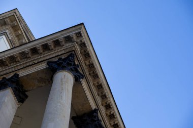 Korint sütunları ve zengin dekore edilmiş antablatür gösteren neoklasik bir binanın alçak açılı görüntüsü. Açık mavi gökyüzü karşıtlık ve açıklık yaratır