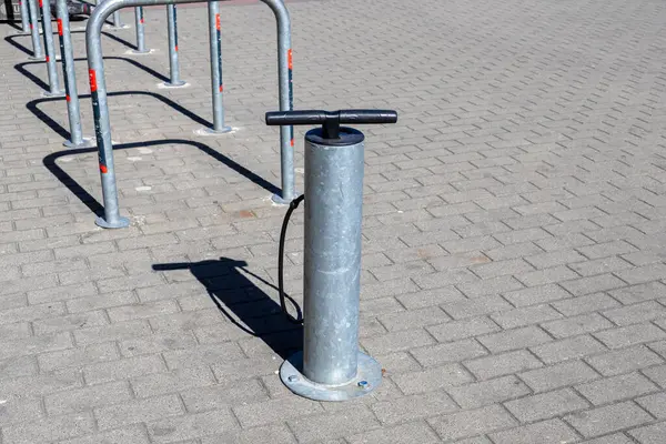 Kaldırım kenarındaki bisiklet raflarının yanına siyah bir hortum takılmış sağlam metal bisiklet pompası. Parlak gün ışığında bisikletçiler için kentsel altyapı