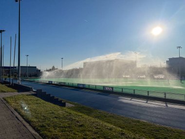 Poznan, Polonya - 02 Nisan 2025: Suni çim sahası güneşli bir stadyumda yüksek basınçlı fıskiyelerle sulanıyor. Sahne açık ve açık bir gökyüzü içeriyor.