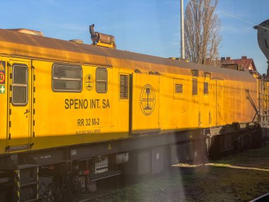 Konin, Polonya - Nisan 04, 2025: Sanayi SPENO RR 32 M-2 demiryolu bakım aracı demiryolu kenarına park edilmiş durumda. Sarı gövde ve logolar gün ışığında görünür.