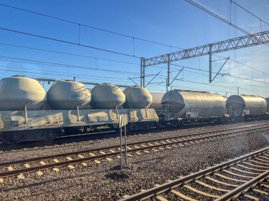 Konin, Polonya - 04 Nisan 2025: Silindirik tank vagonları demiryolu hattının altındaki beton tezgahlarda yüklendi. Parlak gün ışığı sanayi taşımacılığını vurguluyor