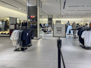 Poznan, Polonya - Nisan 02. 2025: Modern giyim mağazasının iç dekorasyonu şık bir şekilde düzenlenmiş günlük giysi rafları içeriyor. İki dilli bir işaret çıkış için kuyruk yönünü gösterir