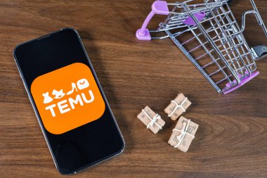 Poznan, Polonya - 26 Mart 2025: Minyatür paketlerin yanında akıllı telefon uygulaması logosu ve küresel online alışveriş, dağıtım ve e-ticaret eğilimlerini temsil eden uçlu bir alışveriş arabası
