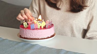 Bir kadın dikkatlice mektup şeklinde doğum günü mumlarını bir kibrit çöpü kullanarak pembe bir pasta üzerinde tutuşturuyor. Sıcak bir aydınlatma ve şenlikli bir atmosferle neşeli bir kutlama hazırlıyor.