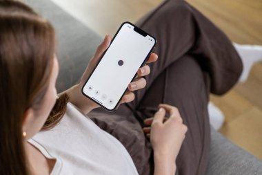 Poznan, Polonya 14 Nisan 2025: Bir kadın telefonundaki yapay zeka asistanıyla minimalist karanlık daire UI ile iletişim kuruyor 