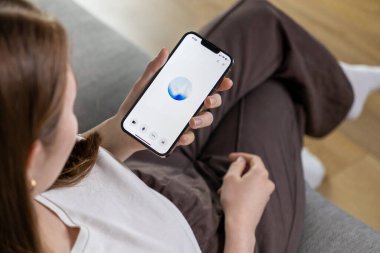 Poznan, Polonya 14 Nisan 2025: Bir kadın cep telefonundaki ses girişi yoluyla yapay zeka asistanıyla etkileşime girer ve minimum arayüzde mavi bir animasyon çemberi gösterir 