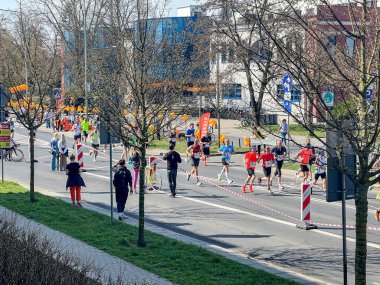 Poznan, Polonya - 13 Nisan 2025: İzleyiciler ve turuncu süslemeler güzergahı kaplarken, işaretli bir şehir yolunda birlikte koşan çeşitli sporcular grubu