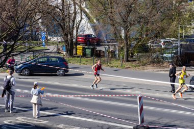 Poznan, Polonya - 13 Nisan 2025: Etkinliğin arka planında izleyiciler ve araçların görüldüğü bir maraton yarışı sırasında işaretli bir şehir yolunda koşan sporcular