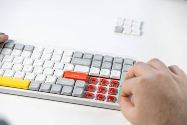 Kişinin elleri kırmızı anahtarları, özelleştirme ve kullanıcı deneyimini ortaya çıkarmak için kaldırılan renkli tuşları gösteren kompakt mekanik bir klavye ile etkileşime girer