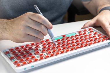Bir kişinin mekanik klavyedeki kırmızı düğmeleri kontrol etmek için çoklu metre ya da test sondası kullanarak, bakım, kalite kontrolü ya da özel montaj sürecini gösteren yakın plan görüntüsü
