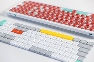 Bir mekanik klavye kurulumu, görünür kırmızı düğmeleri olan ve DIY kiplerini ve kişiselleştirilmiş tasarımı vurgulayan, parçalanmış bir panonun yanına dizilmiş canlı özel tuş kapaklarını gösterir