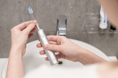 Poznan, Polonya - 27 Nisan 2025: Lavabonun üzerinde gümüş bir Laifen Dalgalı Elektrikli Diş fırçası tutan ellerin yakınlaştırılması, günlük oral bakım rutinine yenilikçi yaklaşımı vurguluyor