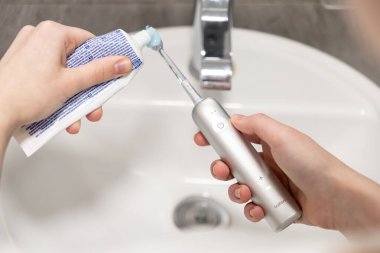 Poznan, Polonya - 27 Nisan 2025: Laifen modern elektrikli diş fırçasına diş macunu süren ellerin yakın çekim görüntüsü bir banyo lavabosunun üzerinde, odaklanmış günlük ağız bakımı rutinini gösteriyor