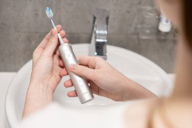 Poznan, Polonya - 27 Nisan 2025: Eller Laifen elektrikli diş fırçasını banyo lavabosunun üzerinde tutuyor, gelişmiş diş sağlığı ve diş sağlığı için modern teknolojiyi vurguluyor