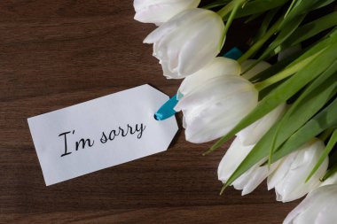 Üzüntü ve sempati anlamına gelen bir kâğıt notun yanında beyaz lale düzenlemesinin genel görünümü zor duygular ya da taziyeleri ifade etmek için mükemmel.